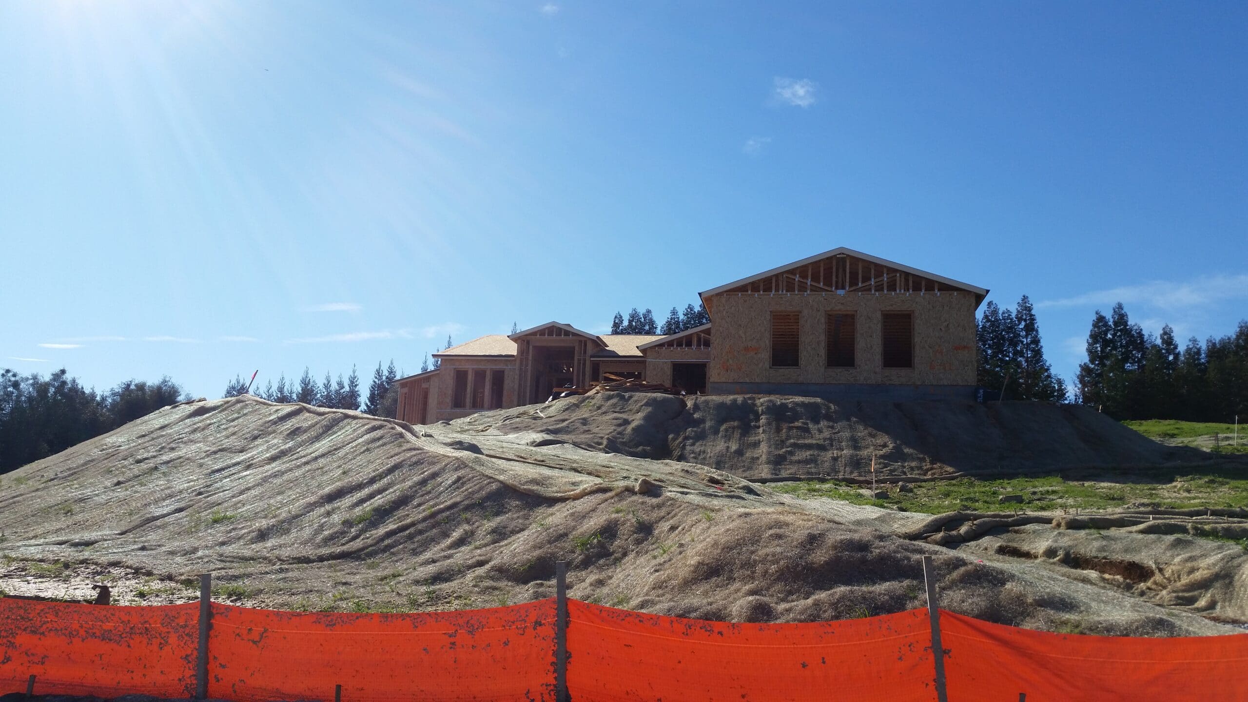 Hill Country Texas custom home under construction showing stone exterior, metal roof, and scenic oak trees